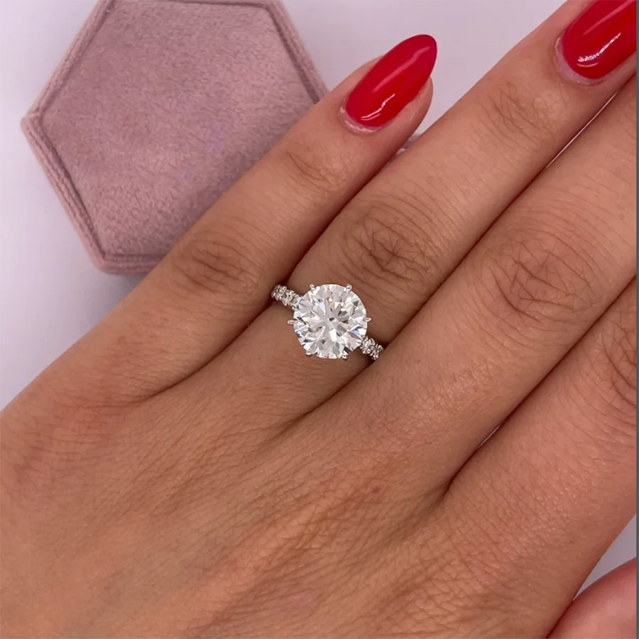 Diamond ring on a hand with red nail polish and a pink jewelry box in the background